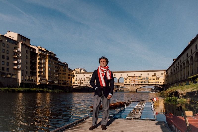 A male model in a red and white scarf stands on a wooden jetty at the edge of a river, in a photo captured with a Canon RF 24-105mm F2.8L IS USM Z lens.  