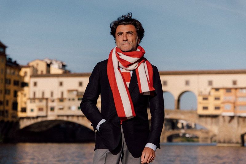 A man in a blazer and red-and-white scarf is captured in sharp focus in front of the softly blurred Ponte Vecchio, in a photo captured with a Canon RF 24-105mm F2.8L IS USM Z lens.