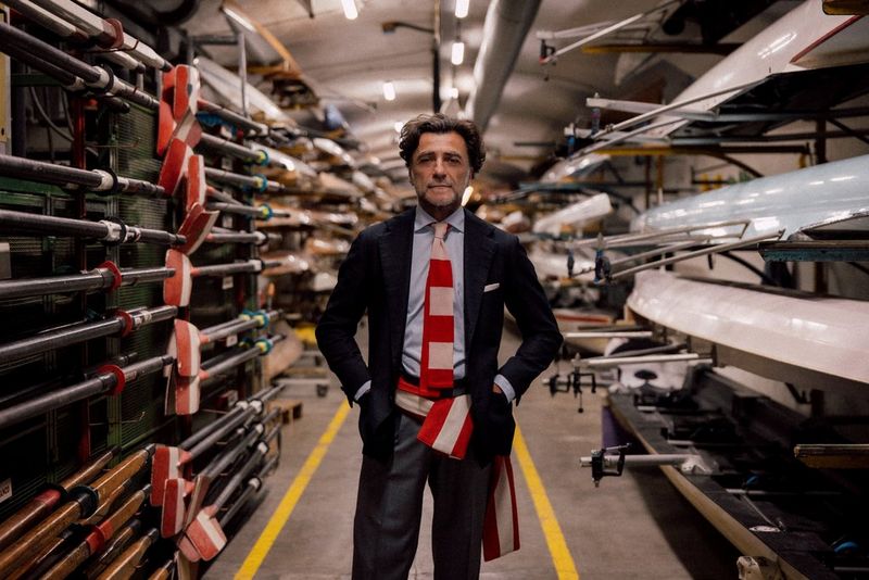 A male model stands, hands in pockets, in between rows of canoes and oars, in an indoor photo captured with a Canon RF 24-105mm F2.8L IS USM Z lens.