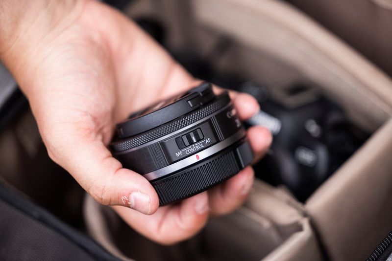 Человек держит в руке объектив Canon RF 28mm F2.8 STM над камерой.
