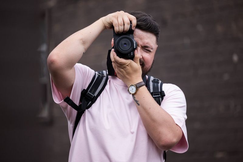 Мужчина держит камеру Canon с фикс-объективом Canon на уровне глаз, пытаясь сделать снимок.