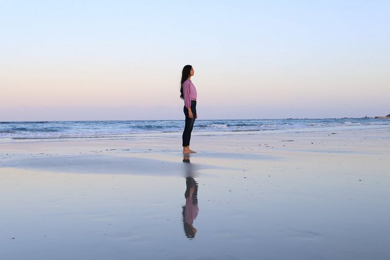 A photography of a woman standing on a beach at sunset, taken on an Canon EOS R7 camera.