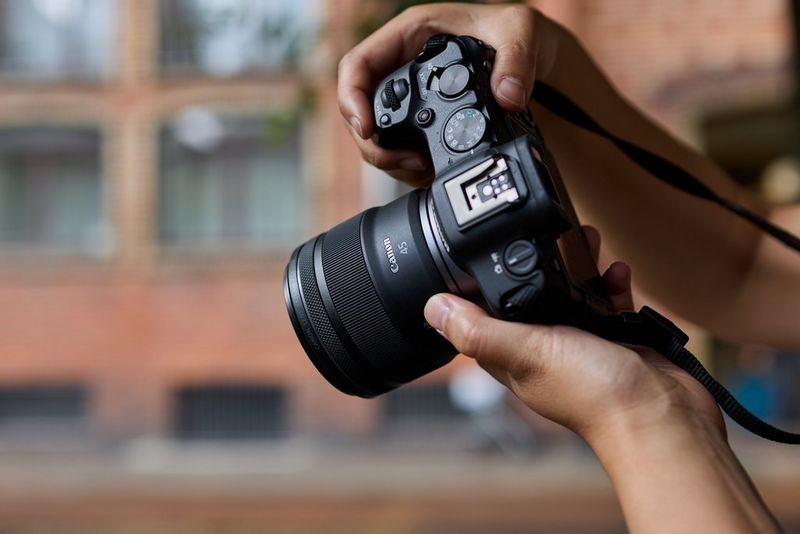 A Canon RF 45mm F1.2 STM lens being used in an urban setting, blurred buildings in the background.