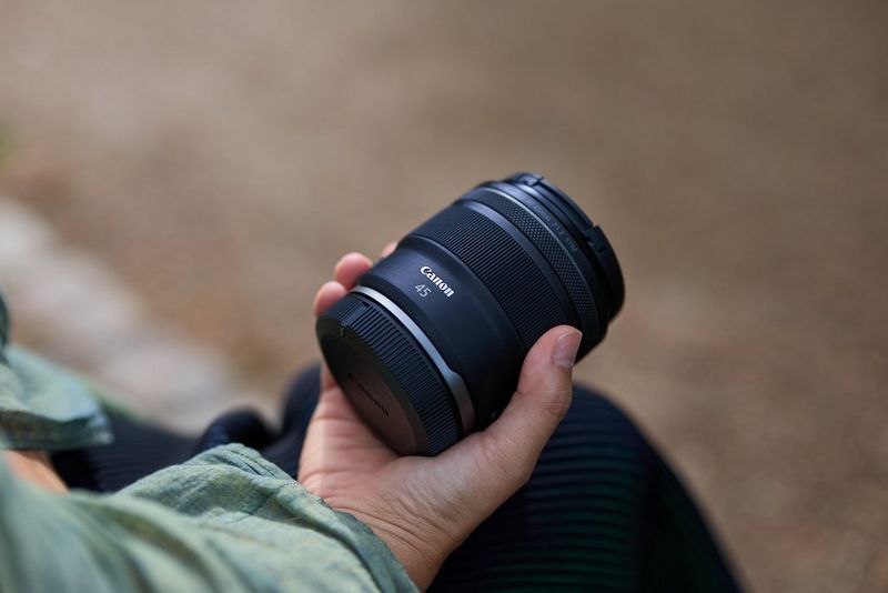 A hand holding a Canon RF 45mm F1.2 STM prime lens.