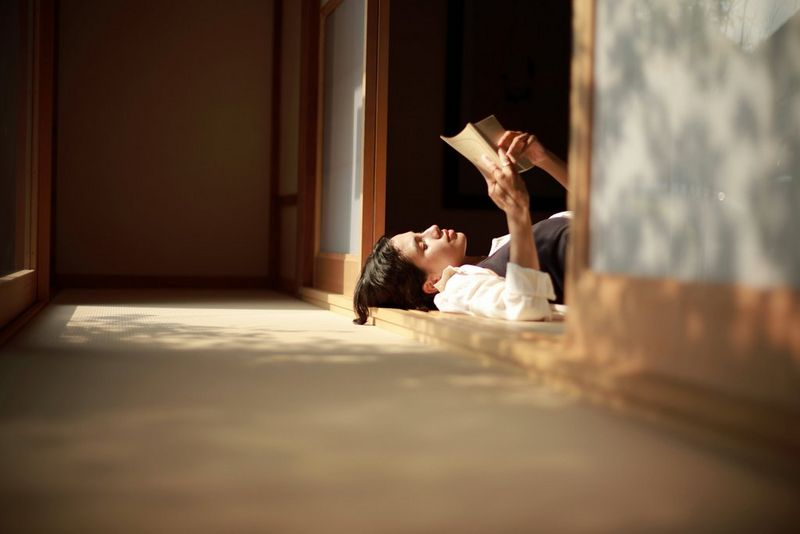 A portrait taken with the Canon RF 45mm F1.2 STM lens, showing a woman led on her back in a doorway, reading a book held above her head.