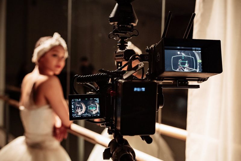 Een Canon-camera op een statief, waarmee een ballerina wordt gefilmd die een witte tutu en wit accessoire op haar hoofd draagt. Op het scherm van de camera zijn cirkelvormige fisheye VR-beelden te zien die zijn gemaakt met het Canon RF 5.2m F2.8L DUAL FISHEYE-objectief dat op de camera is bevestigd.
