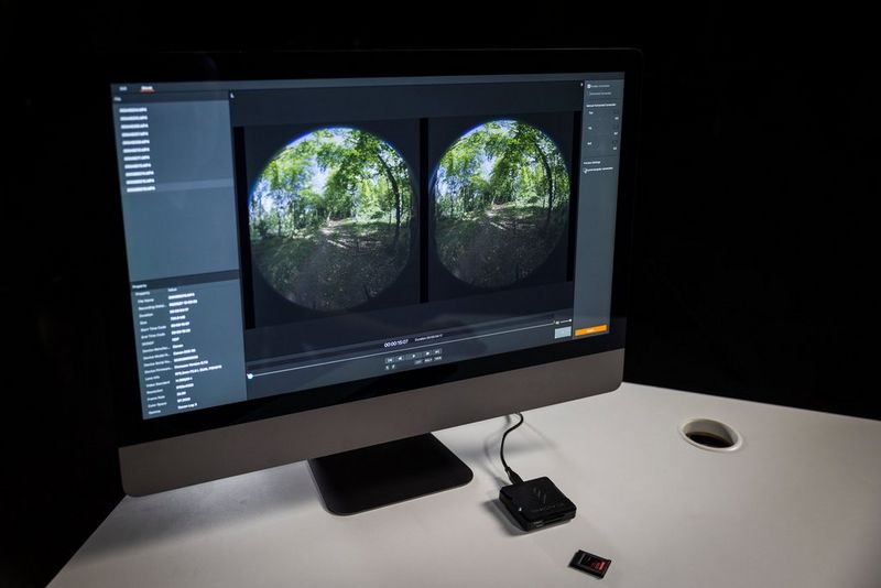Een computerscherm met daarop twee cirkelvormige beelden van een bospad, die zijn vastgelegd met een VR-objectief. Het scherm staat op een wit bureau en er is een geheugenkaartlezer op aangesloten.