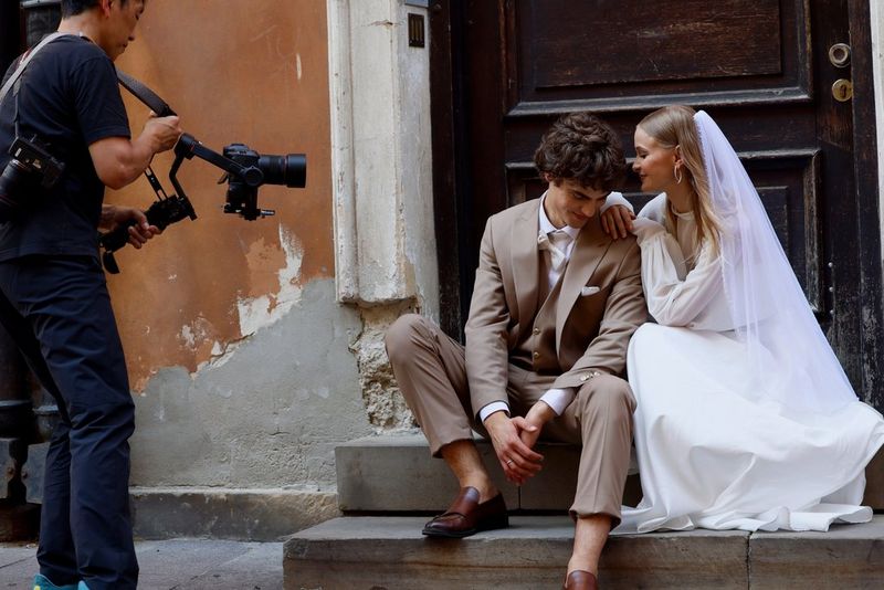 Una sposa e uno sposo seduti su uno scalino, con una fotografa che utilizza un obiettivo Canon RF 50mm F1.4 L VCM per catturare un momento intimo tra loro.