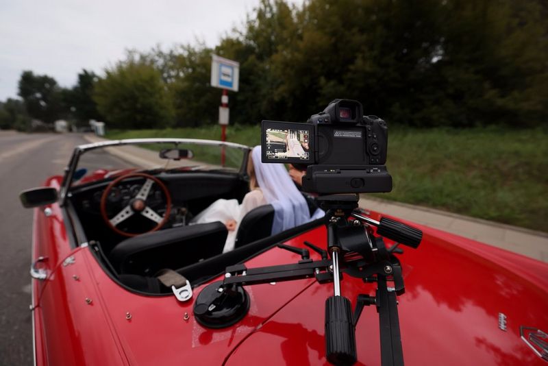 A close-up of a Canon camera with a Canon RF-50mm-F1-4L-VCM lens filming a seated man, just visible out of focus in the background.