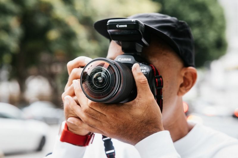 Professional photographer Atiba Jefferson raises a Canon EOS R5 Mark II equipped with an RF 7-14MM F2.8-3.5L FISHEYE STM lens to his eye.