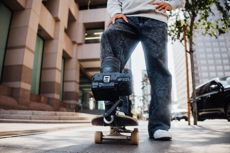 Ein Mann steht mit einem Fuss auf einem Skateboard, an das eine Canon EOS C50 mit einem RF 7-14mm F2.8-3.5L FISHEYE STM Objektiv angeklemmt wurde.