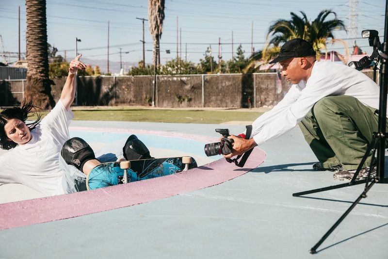 Photographer Atiba Jefferson crouches low with a Canon EOS R5 Mark II and Canon RF 7-14mm F2.8-3.5L FISHEYE STM lens, shooting a skateboarder at the lip of a concrete bowl.