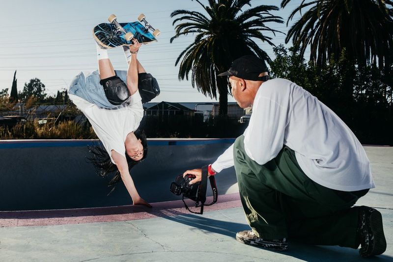 Atiba Jefferson holding an EOS R5 Mark II and RF 7-14MM F2.8-3.5L FISHEYE STM lens close to the edge of a concrete bowl, where a skateboarder is doing a handplant.