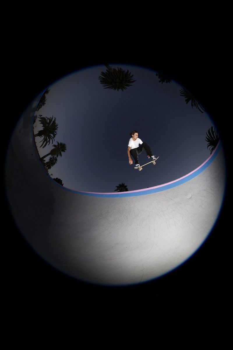 A skateboarder, frozen by flash from a Speedlite in mid-air above a concrete bowl and captured in a circular fisheye image.