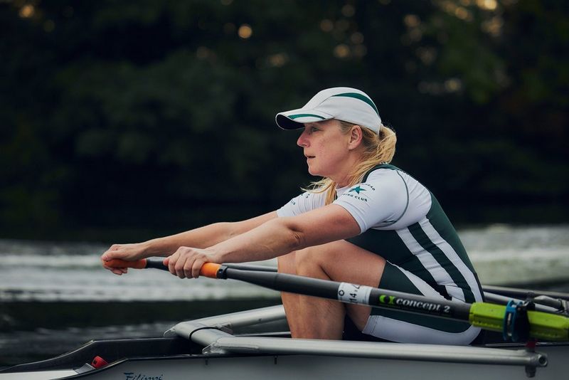 Een roeier leunt naar voren op de riemen. Er is scherp ingesteld op de atleet, terwijl de achtergrond vaag is.