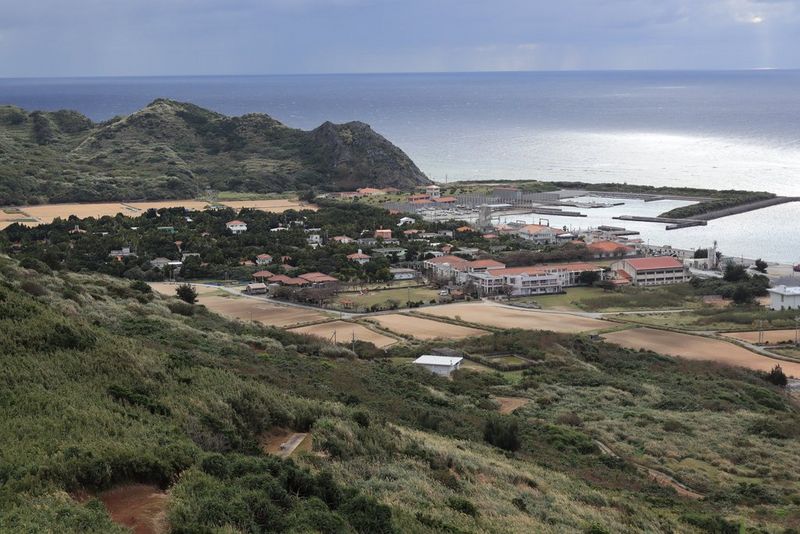 Imagen tomada a una longitud focal de 45 mm que muestra una ensenada en la costa, con una zona verde en primer plano y unos edificios a media distancia.