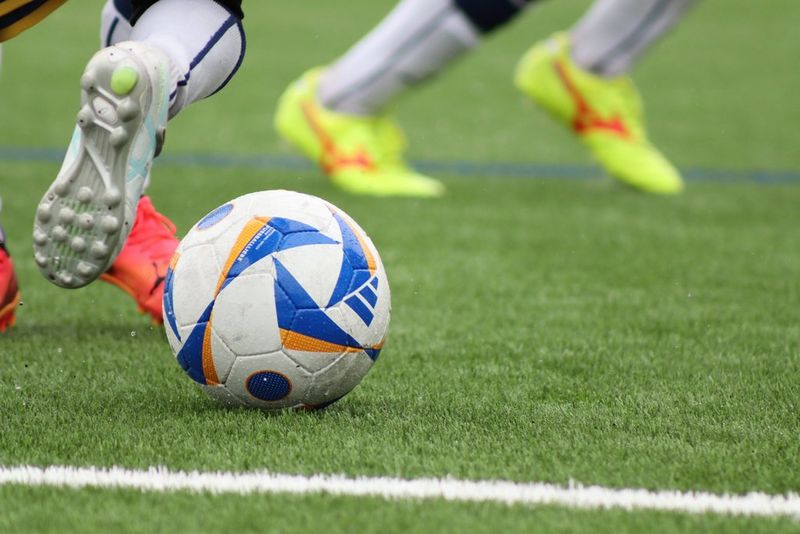 A tight crop of a football at players' feet during a match, captured using the long end of a Canon RF 75-300mm F4-5.6 lens.