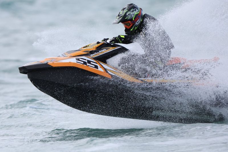 A jet ski powering across the water's surface at speed, spray covering the rider. Action sports photo taken with a Canon RF 800mm F5.6L IS USM lens.