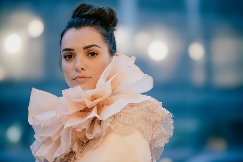 Un'immagine scattata in condizioni di scarsa illuminazione di un modello in un colletto con volant in posa davanti a lampioni sfocati. Scatto realizzato con Canon EOS R e obiettivo Canon RF 85mm F1.2L USM DS.