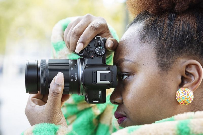 Користувач підносить до ока камеру Canon EOS R50 з об’єктивом Canon RF-S 55-210mm F5-7.1 IS STM, тримаючи одну руку на кнопці затвора, а іншу — на кільці трансфокатора об’єктива.