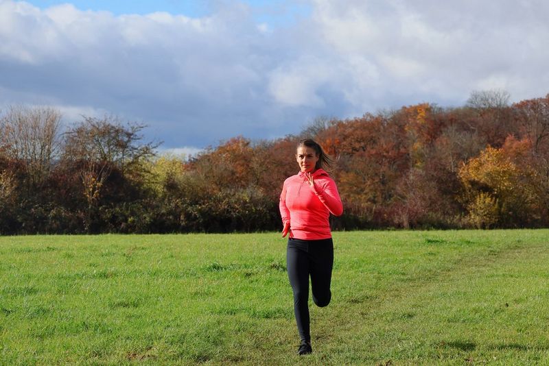 A woman runs across the grass towards the camera, autumn trees in the background. Action photo taken with a Canon RF-S 55-210mm F5-7.1 IS STM lens.