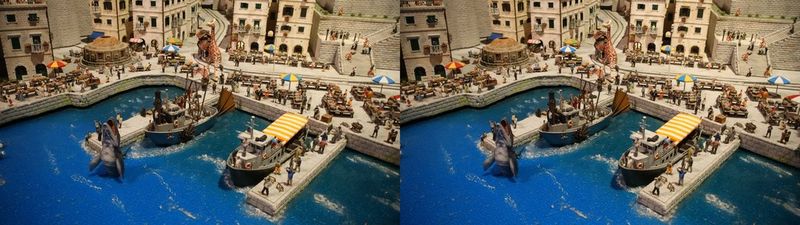 Una coppia di immagini stereoscopiche raffiguranti una città in miniatura, con barche, piccole figure sparse su un molo fittizio e uno squalo che salta dalle vivaci acque blu. Scatto realizzato con obiettivo Canon RF-S 7.8mm F4 STM DUAL.