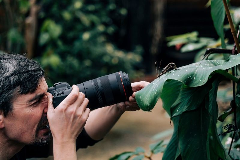A man uses a camera with a large lens to take a close-up photograph of an insect on a leaf.