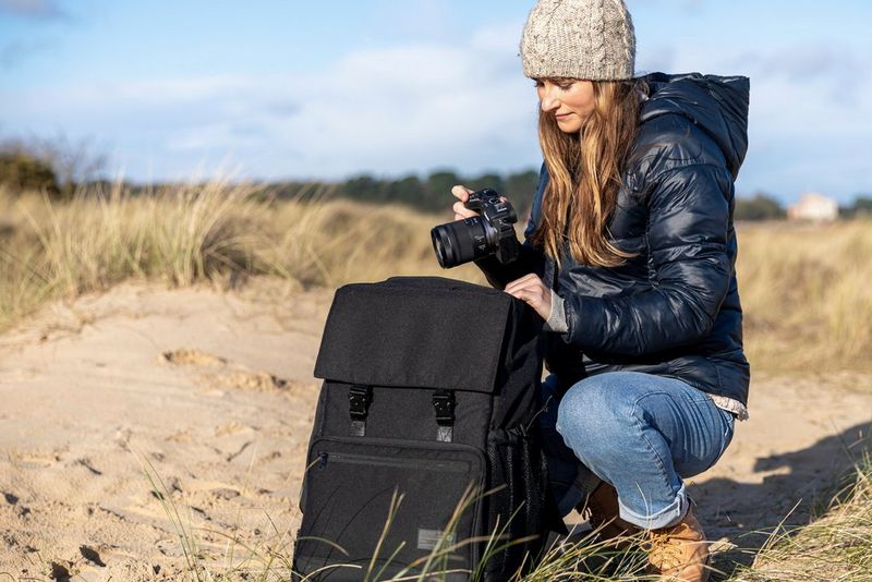A woman crouches on a sandy beach to put a Canon camera in her kitbag.
