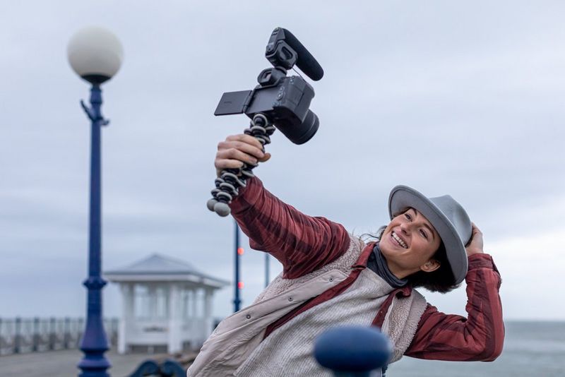 A photographer films herself on a windswept pier with a Canon camera with a microphone and windscreen attached.