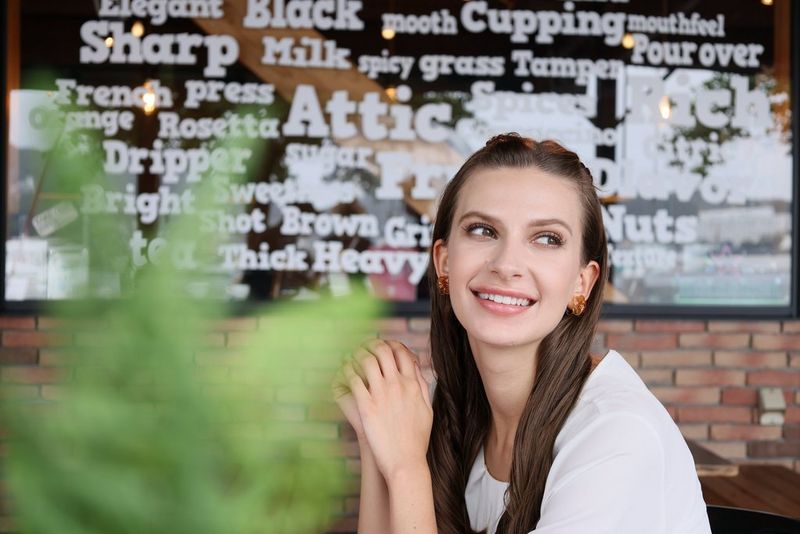 Portretfoto van een vrouw voor een toonbank in een café, gemaakt met een Canon RF 24-105mm F4-7.1 IS STM-lens. Een plant op de voorgrond is onscherp, maar de woorden achter haar zijn nog steeds goed leesbaar.
