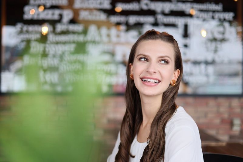 Portretfoto van een vrouw voor een toonbank in een café, gemaakt met een Canon RF 50mm F1.8 STM-lens met een groot diafragma. Een plant op de voorgrond en woorden en het metselwerk op de achtergrond zijn onscherp.