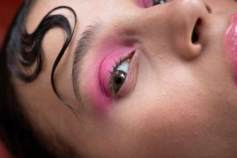 Крупный план той же женщины с ярко-розовыми тенями на веках.