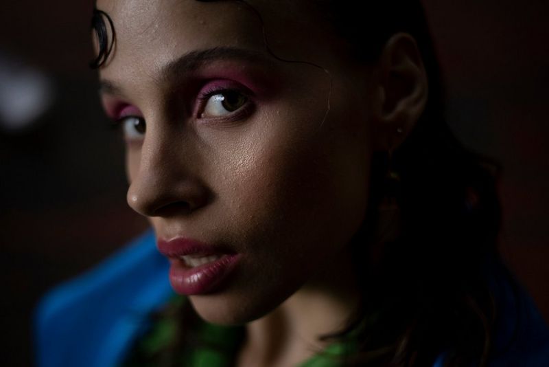Крупный план запечатленного при слабом освещении лица женщины с темными волосами и макияжем — розовой помадой и тенями для глаз.