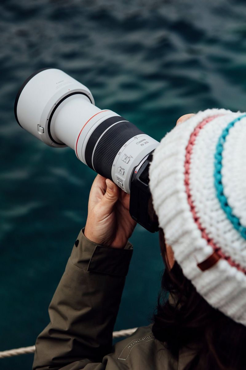 Een vrouw, van achteren gezien, draagt een wollen hoed en houdt een Canon EOS R System-camera met een Canon RF 70-200mm F4L IS USM-lens vast.