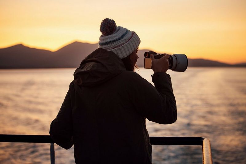 La fotografa Lucia Griggi a poppa di un'imbarcazione, con la fotocamera in mano, di fronte a un suggestivo tramonto.