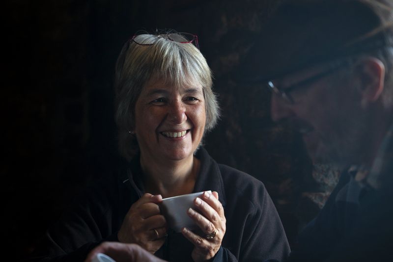 Ritratto in condizioni di scarsa illuminazione di una donna che tiene in mano una tazza e sorride al suo compagno.