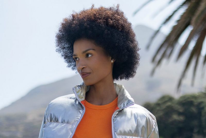Portretfoto buiten van een vrouw met een afrokapsel, met een spitse bergtop, groen en de bladeren van een palmboom onscherp op de achtergrond, gemaakt met een Canon RF 50mm F1.8 STM-lens.