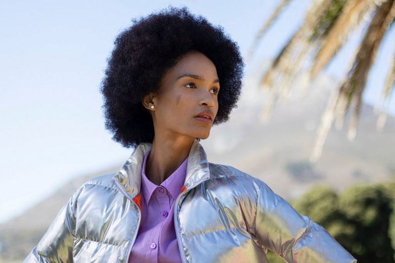 Photo de portrait en extérieur d'une femme à la coupe afro, avec un sommet de montagne escarpé, de la végétation et les feuilles d'un palmier, tous flous en arrière-plan, prise avec un objectif Canon RF 50mm F1.8 STM.