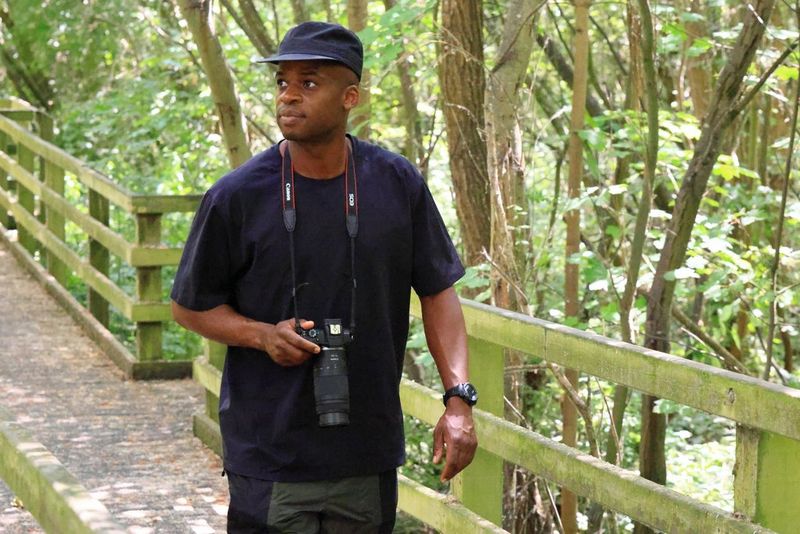 Bird enthusiast Ollie Olanipekun walking along a woodland path, holding a Canon EOS R100 and RF 75-300mm F4-5.6 lens.
