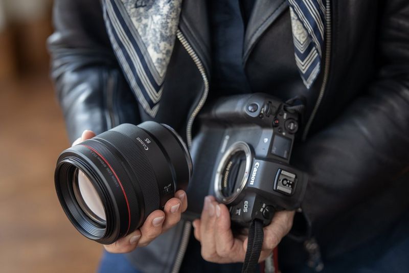 Iemand houdt een Canon-camera in de ene hand en een RF-objectief in de andere, alsof de persoon op het punt staat dit op de camera te monteren.