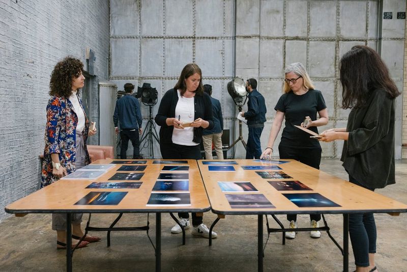Quatre femmes se tiennent autour de deux tables à tréteaux et discutent des images disposées devant elles.