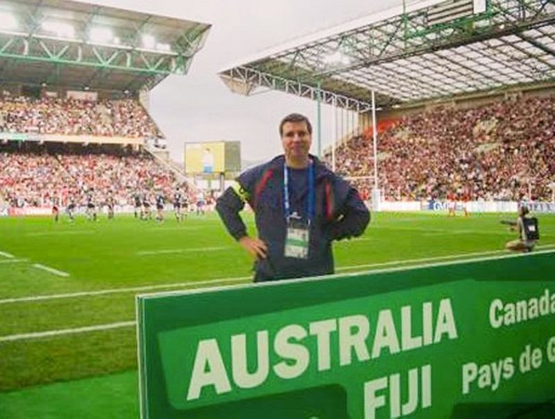 João Granite’s father, wearing a tracksuit and a lanyard, stands at the side of a pitch in a full stadium