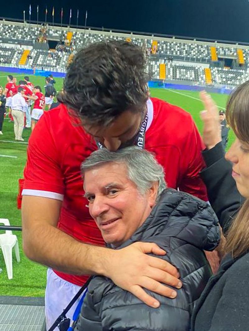 João Granite, wearing a red Portugal jersey, kisses his father’s head at the side of a rugby pitch
