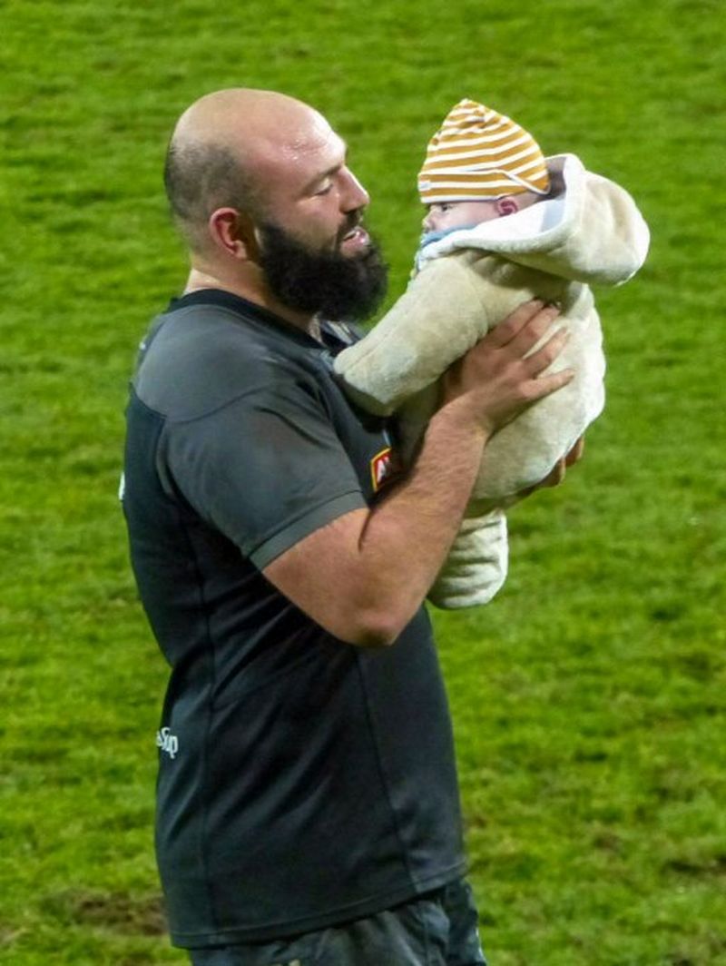 Mike Tadjer holds his young son affectionately on a rugby pitch