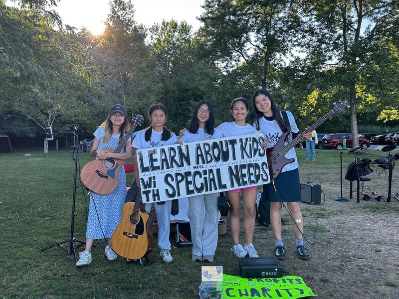 Five girls holding guitars stand behind a banner reading ‘learn about kids with special needs’.