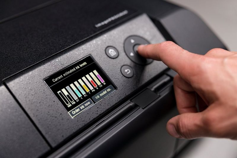 Een gebruiker drukt op de knop OK op de voorkant van een Canon imagePROGRAF PRO-300-printer terwijl op het LCD-scherm de inktniveaus staan.