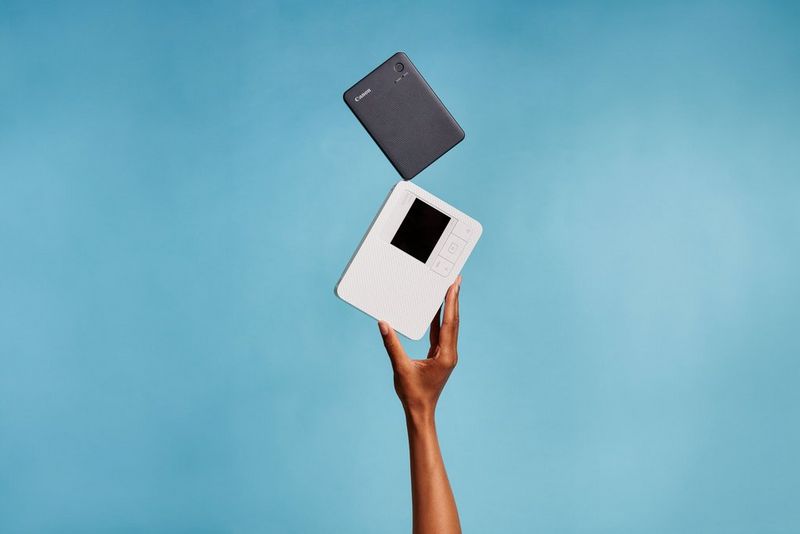 Two Canon SELPHY CP1500 printers sit next to two Canon SELPHY Square QX10 printers on a bright pink background.