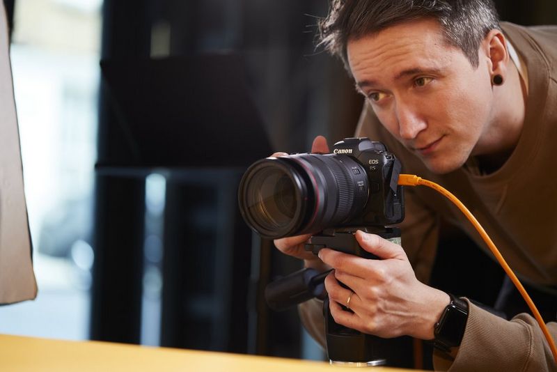 A man observes a product while handling a Canon R5 camera, connected by ethernet for an easier production workflow.