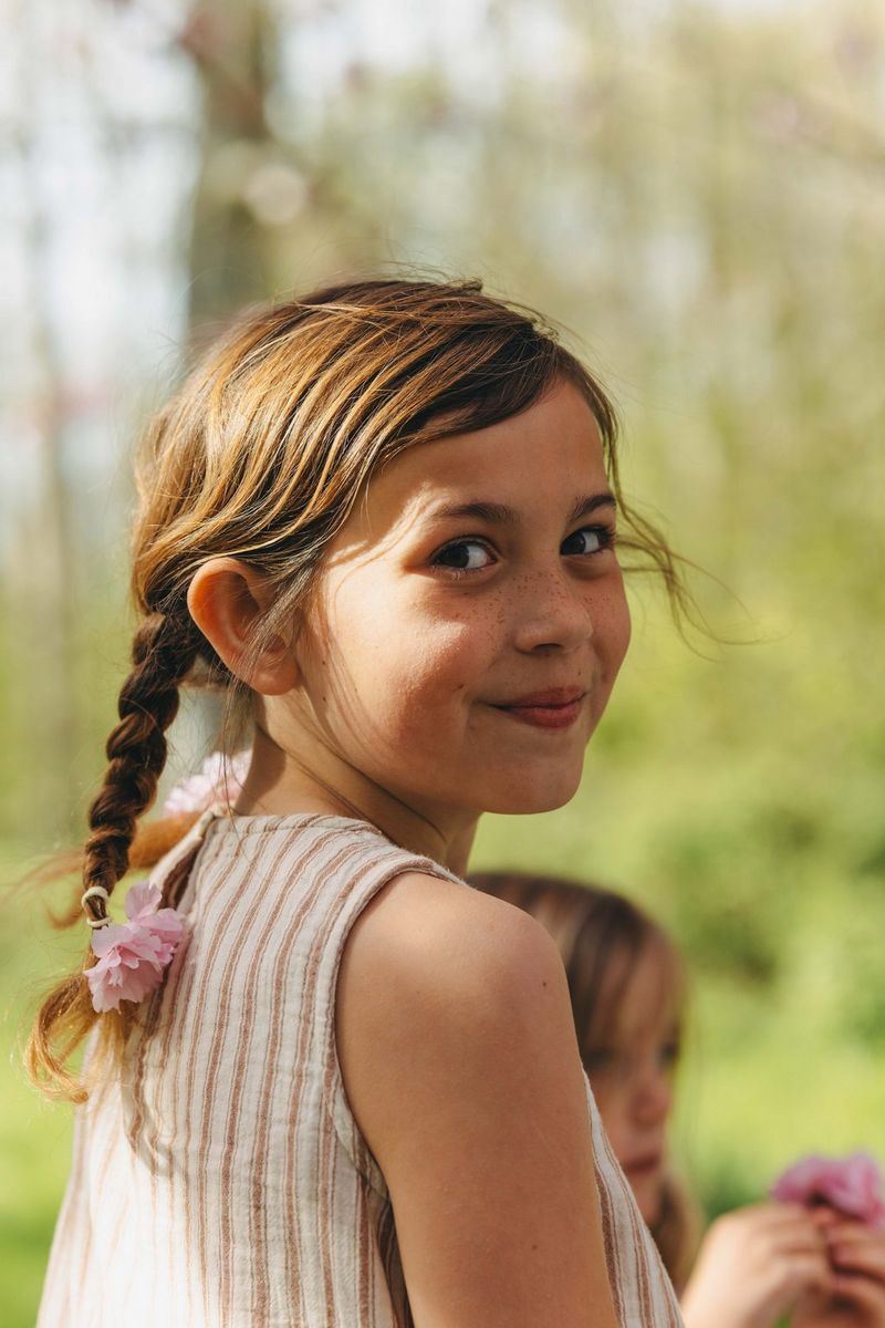 A close-up portrait of a child looking toward the camera, with cherry blossoms and greenery softly blurred in the background.