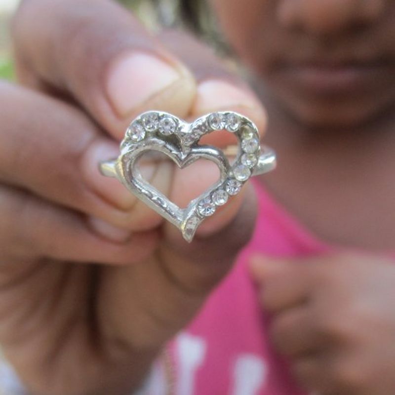 A hand holding a heart-shaped silver sparkly broach